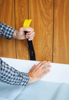 a man is using scissors to cut paper on the wall with wood paneling behind him