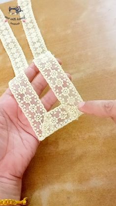 a hand holding two pieces of lace on top of a wooden table next to a yellow beaded bracelet