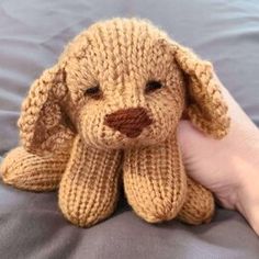 a hand holding a stuffed dog on top of a bed