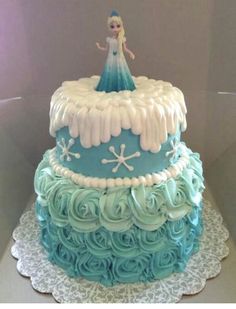 a three tiered cake decorated with blue frosting and white icing, has a frozen princess figure on top