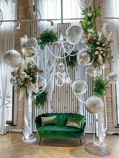 a green couch sitting under a chandelier filled with disco balls and greenery