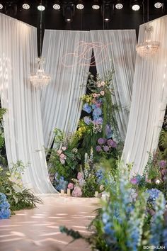 an outdoor wedding setup with flowers and chandelier hanging from the ceiling, surrounded by white drapes