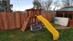 a yellow slide in the yard next to a wooden fence