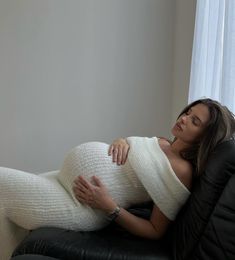 a pregnant woman laying on top of a black leather chair in front of a window