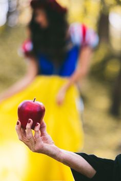 a person holding an apple in front of a woman wearing a yellow dress and red hat