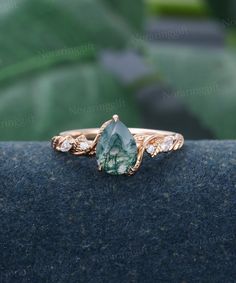 a green and white stone ring on top of a black surface with leaves in the background