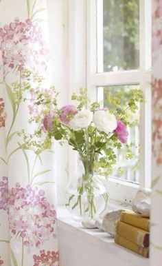 a vase filled with flowers sitting on top of a window sill next to a curtain