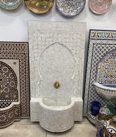 a white marble fountain surrounded by plates and bowls on display in a room with tile walls