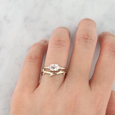 a woman's hand wearing a gold ring with two diamonds on it and a white marble background