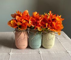 three mason jars with orange flowers in them on a tableclothed cloth covered table