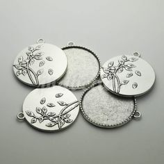 four silver plated pendants with flowers and leaves on each one, set against a gray background