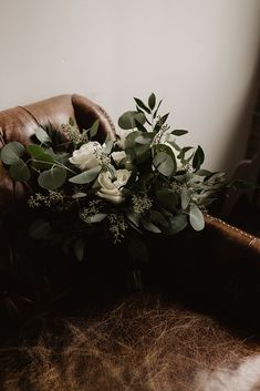 a bouquet of white flowers sitting on top of a brown leather chair next to a window