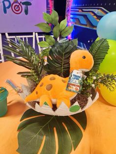 a toy dinosaur in a planter on top of a table with balloons and streamers