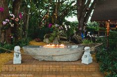 a fire pit sitting on top of a brick walkway next to trees and flowers in the background