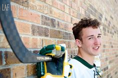 a young man standing next to a brick wall holding a pair of drillers and smiling at the camera