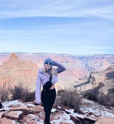 a woman standing on top of a snow covered mountain next to the grand canyon in winter