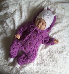 a baby wearing a purple knitted outfit laying on top of a white blanket next to a stuffed animal