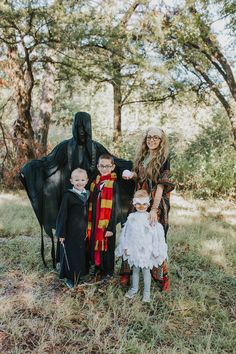 three children in halloween costumes standing next to a black horse with two adults and one child