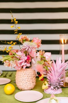 the table is set with pineapples, pink flowers and yellow candlesticks