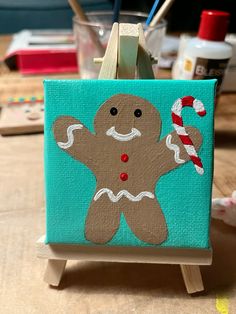 a wooden easel with a painting of a gingerbread man holding a candy cane