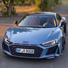 a blue sports car parked on the side of a road next to a tree filled field