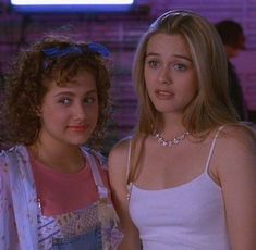 two young women standing next to each other in front of a brick wall and neon sign