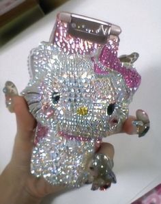 a hand holding a hello kitty phone case with sequins and bows on it