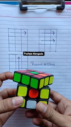 a person holding a rubik cube in their hand next to a piece of paper