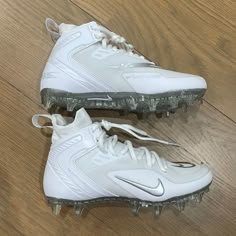 a pair of white nike cleats sitting on top of a wooden floor