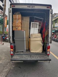 the back end of a moving truck filled with boxes and refrigerators on the street