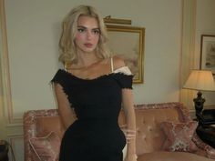 a woman standing in front of a couch wearing a black dress