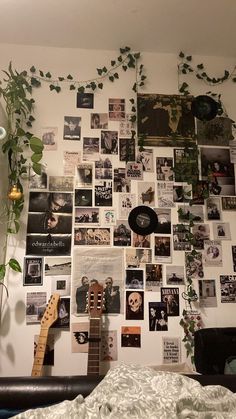 a bedroom wall covered in pictures and plants next to a bed with a guitar on it