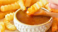 a person dipping some kind of sauce in a bowl with french fries on the side