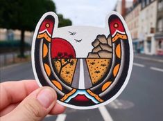 a hand holding up a sticker with an image of two birds on the road