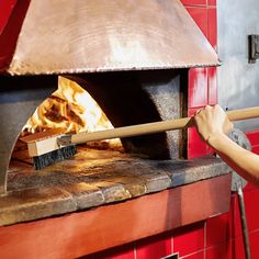 a woman is cleaning the inside of an oven with a broom and fire in it