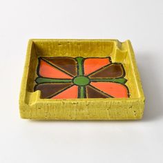 an orange and green tray with a flower on it's side, sitting on a white surface