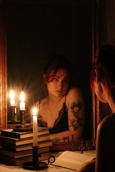 a woman sitting at a table in front of a mirror with books and candles on it