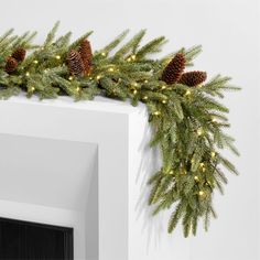 a christmas garland with pine cones and lights hanging from the side of a white fireplace