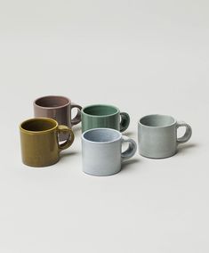 five different colored coffee mugs on a white surface