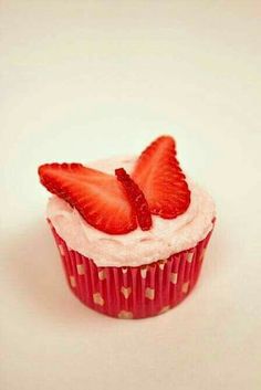 a strawberry cupcake with white frosting and strawberries on top, sitting on a pink surface