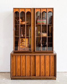 an old wooden china cabinet with glass doors and shelves on the top, in front of a white wall