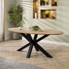 a round table with black cross legs in a living room next to a potted plant