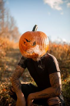 a man sitting in the grass with a pumpkin on his head and tattoos on his arms