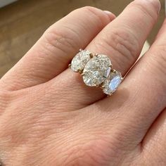 a woman's hand holding an engagement ring with three stones on it and the middle one in yellow gold