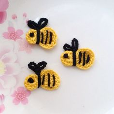 three crocheted bees sitting on top of a white plate next to pink flowers