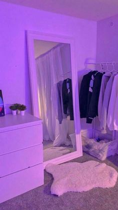 a white dresser sitting next to a mirror in a room with clothes on hangers