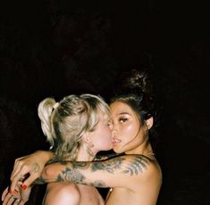 two women are hugging each other while one woman has tattoos on her arm and chest