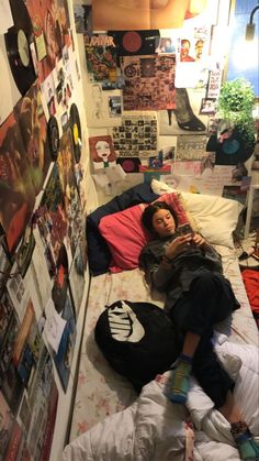 a woman laying on top of a bed next to a wall covered in pictures and posters