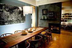 a dining room table with chairs and a large painting on the wall behind it in front of a fire place