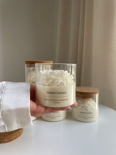 a hand holding a jar of whipped cream next to two jars of whipped cream on a table